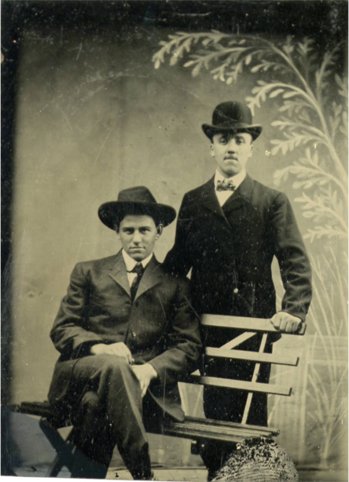 scan of tintype of two men; one seated on wooden bench, one standing behind him resting hand on shoulder
